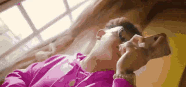 a woman in a pink sweater is laying on a bed looking at her phone .