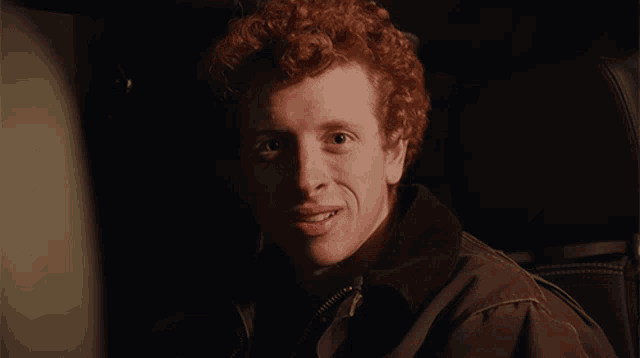 a young man with red curly hair is smiling for the camera