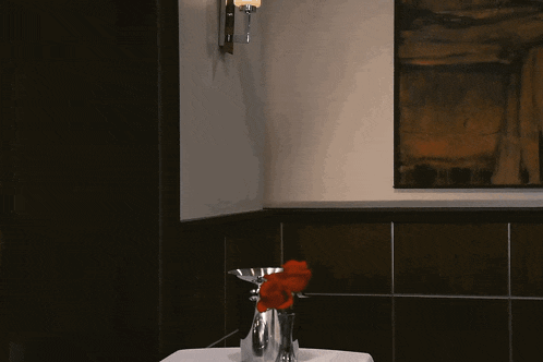 a man peeking out from behind a wall with a vase of red flowers