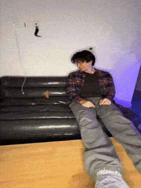 a man in a plaid shirt is sitting on a black couch