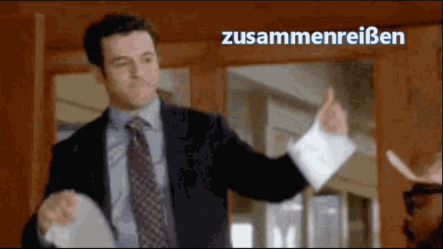a man in a suit and tie is holding a piece of paper in front of a sign that says zusammenreissen