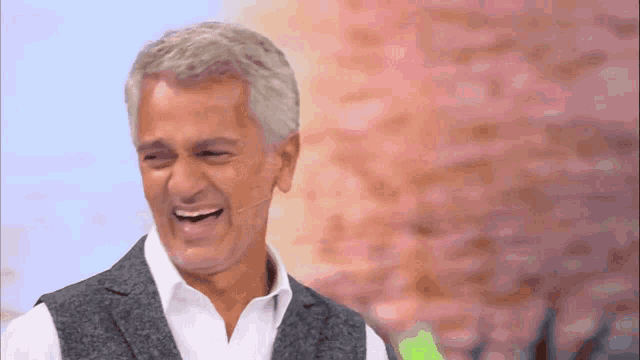 a man in a suit and white shirt is laughing with a microphone in front of him