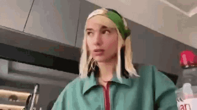 a woman in a green jacket is standing in a kitchen with a bottle of water .