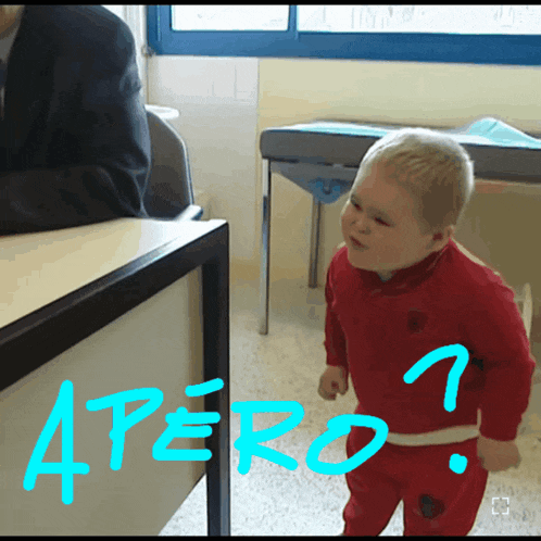 a baby in a red outfit is standing in front of a desk with the word apero written on it