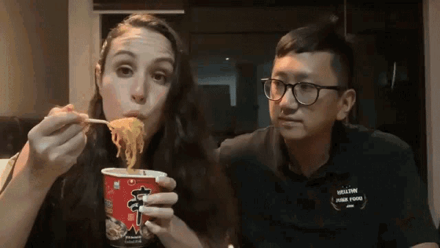 a man and a woman are eating noodles from a cup with chinese writing on it
