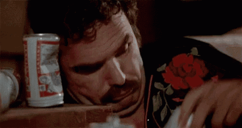 a man with a mustache is holding two budweiser cans in his hands .