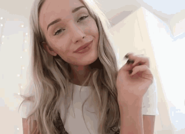 a woman with long blonde hair is smiling and holding a small object