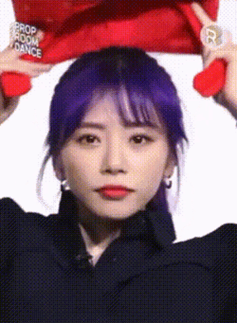 a woman with purple hair is holding a red hat that says prop room dance on it