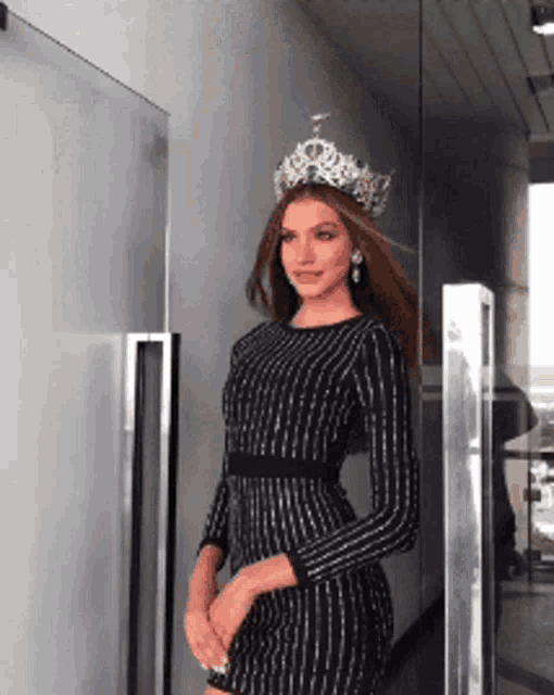 a woman wearing a crown and a striped dress is standing in front of a glass door
