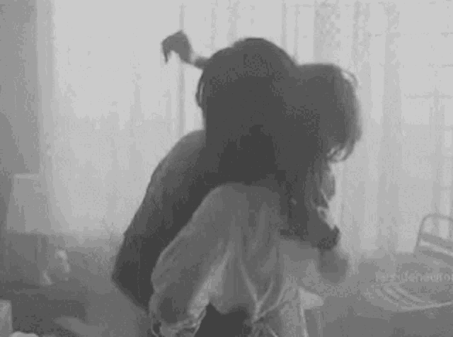a black and white photo of a man and a woman hugging each other in a room .