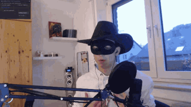 a man wearing a cowboy hat and a mask stands in front of a microphone