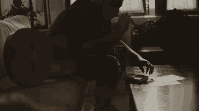 a person sitting on a couch with a guitar in the background writing on a piece of paper