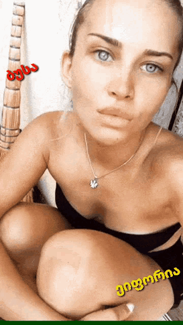 a woman wearing a black top and a necklace is kneeling down in front of a white wall