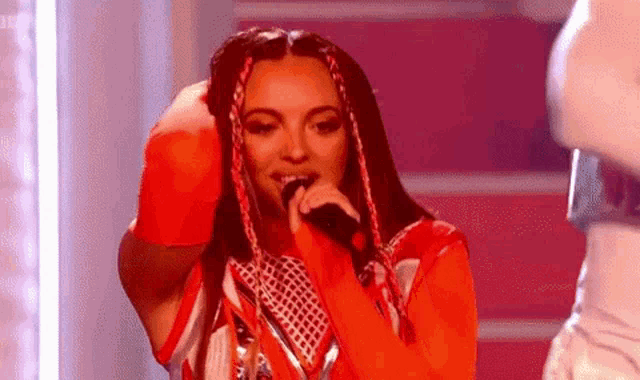 a woman in a red outfit is singing into a microphone on stage .