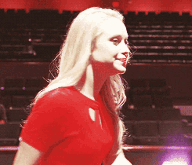 a blonde woman in a red shirt is standing in front of empty rows of seats