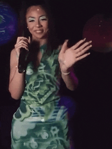 a woman in a green dress is standing in front of a microphone and waving .