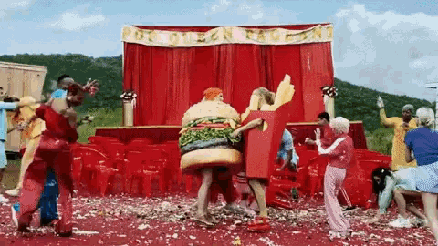 a group of people dressed in food costumes are dancing in front of a sign that says por queen