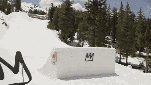 a snowboarder is doing a trick on a snow ramp with the letter m on it