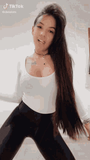 a woman with long hair is wearing a white top and black leggings and dancing .