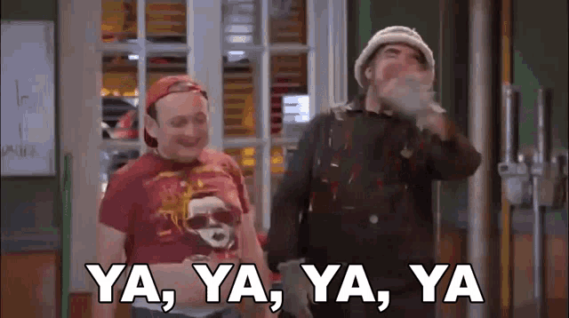 two men are standing next to each other in a room and one of them is smoking a cigarette and the other is laughing .