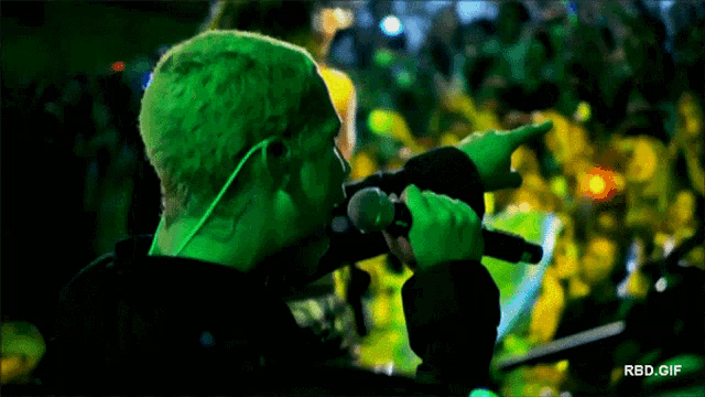a man singing into a microphone with a green background and the words rbd.gif below him