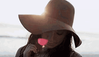 a woman in a hat is holding a glass of wine .
