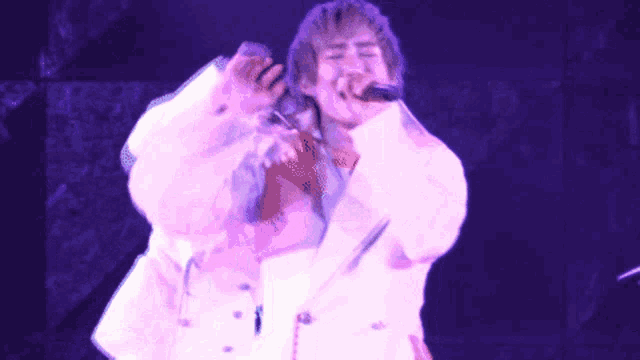 a man singing into a microphone with a pink background