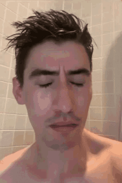 a man without a shirt is taking a shower with his eyes closed