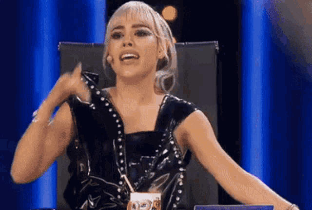 a woman in a black dress is sitting in a chair on a stage with her arms outstretched .