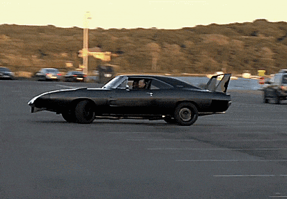 a black car with a spoiler on the back is driving down a parking lot