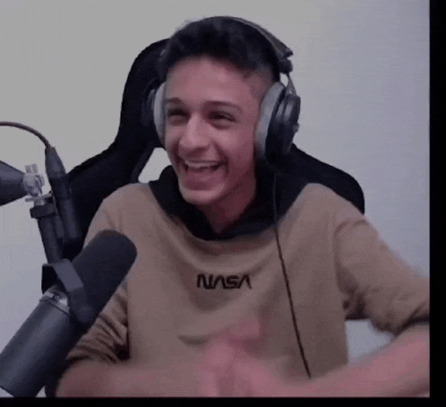 a young man wearing headphones and a nasa shirt is sitting in front of a microphone and smiling .