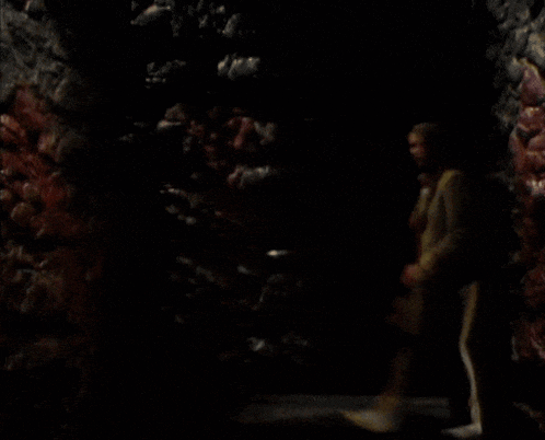 a man in a tan coat and striped pants is standing in a dark cave