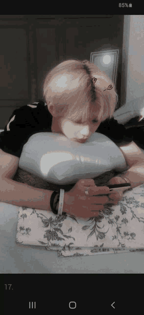 a man laying on a bed with his head on a pillow looking at his cell phone