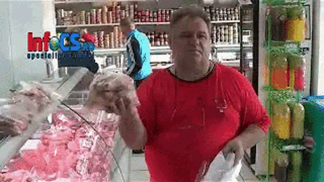 a man in a red shirt is holding a bag of meat in front of a glass display case in a store .