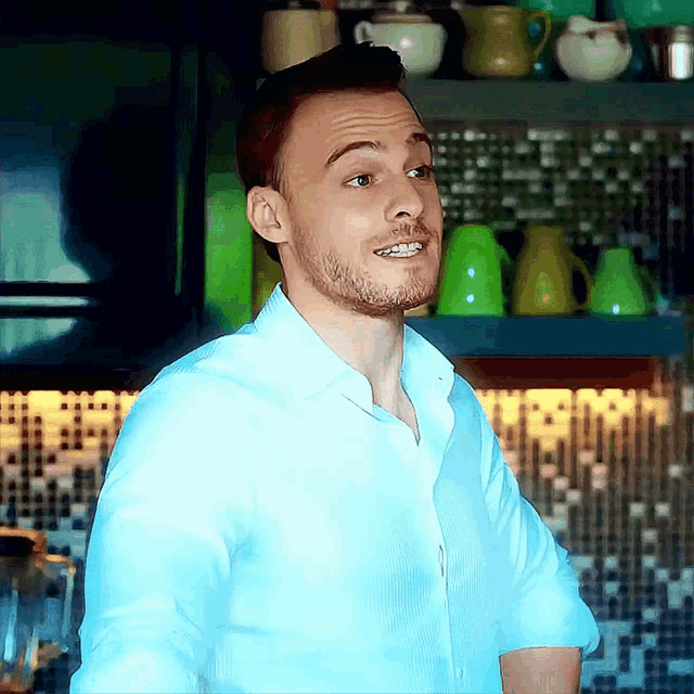 a man in a blue shirt is standing in front of a shelf with cups