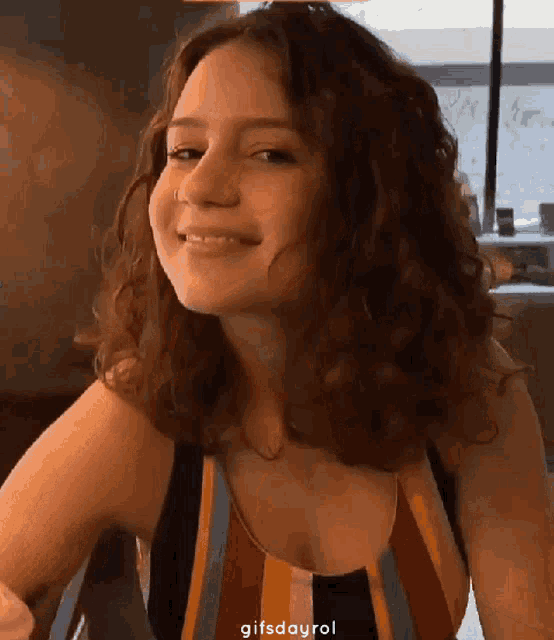 a woman with curly hair wearing a striped tank top smiles