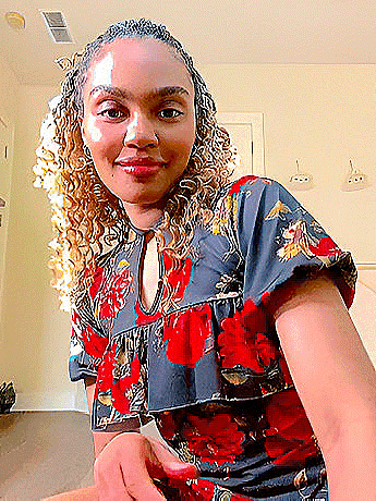 a woman with curly hair is wearing a floral dress and smiling for the camera .
