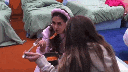 two girls are sitting at a table eating food from a bowl .