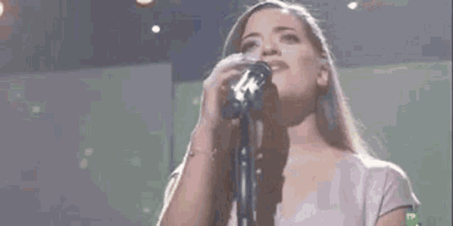a woman is singing into a microphone on a stage in front of a green background .
