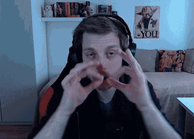 a man wearing headphones looks at the camera with a poster on the wall that says " i love you "