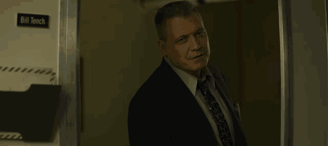 a man in a suit and tie is standing in front of a door that says we might be okay