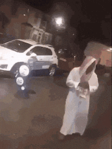 a man in a white robe is walking down the street at night holding a large saw .