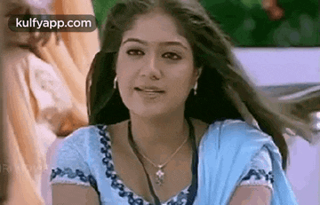 a woman wearing a blue top and a necklace is smiling .