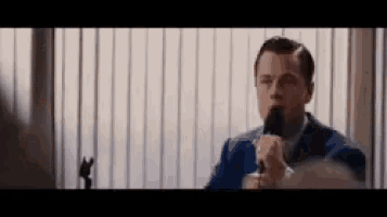 a man in a suit is talking into a microphone while sitting in front of a window .