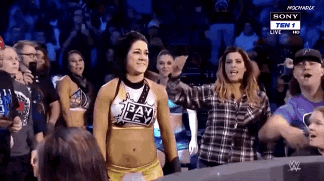 a female wrestler is standing in front of a crowd wearing a bayley shirt .