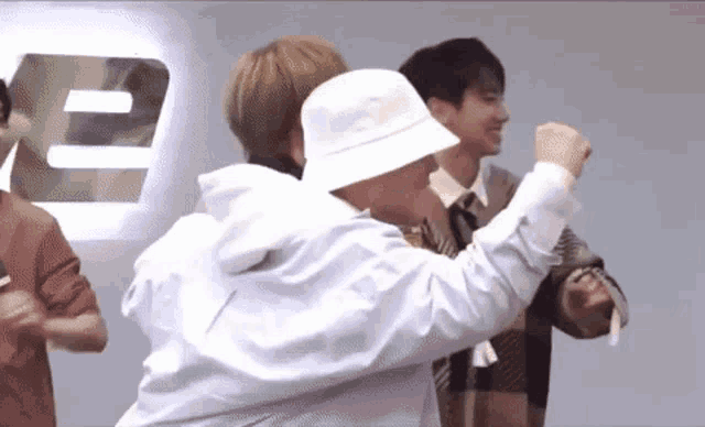 a group of men are standing next to each other in a room and one of them is wearing a white hat .