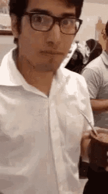 a man wearing glasses and a white shirt is holding a straw in his mouth .