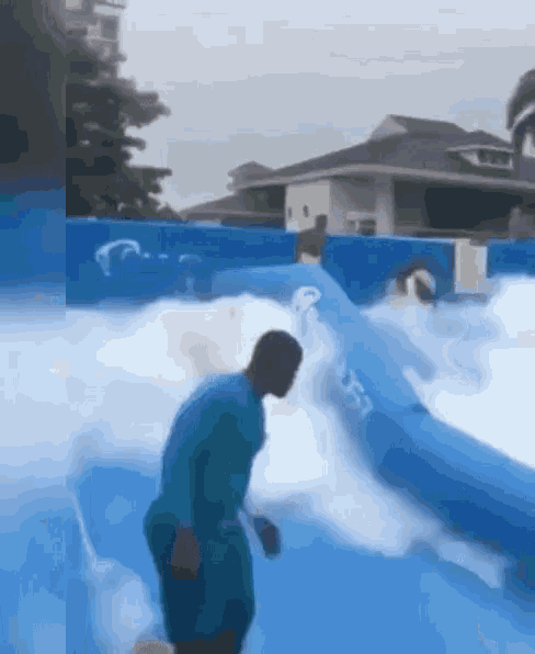 a man in a blue shirt is standing in a pool of water with foam coming out of it .