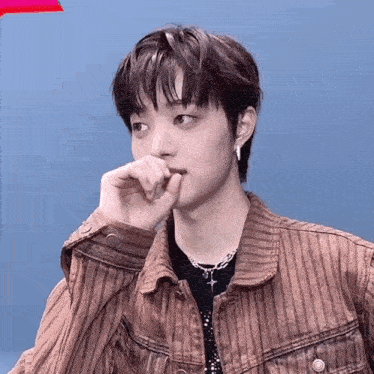a young man wearing a brown striped jacket and a black shirt is covering his mouth with his hand .