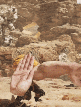 a person 's hand is reaching out towards another person 's arm in the desert